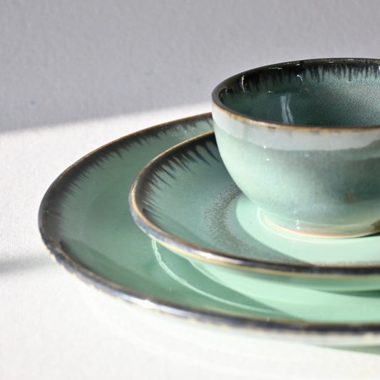 Set of green ceramic plates and bowl from Saabi house on a light surface with a gray background