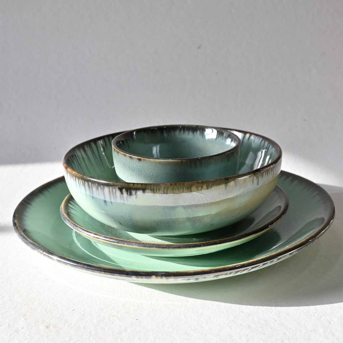 Set of green ceramic dishes on a white surface with a gray background from Saabi House