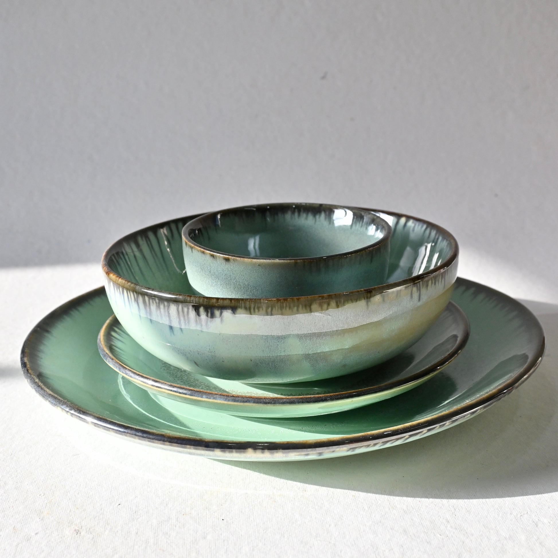 Set of green ceramic dishes on a white surface with a gray background from Saabi House