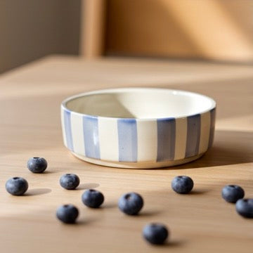 Striped ceramic bowl with blueberries on a wooden surface