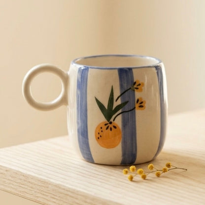 Ceramic mug with striped design and fruit illustration on a wooden surface.