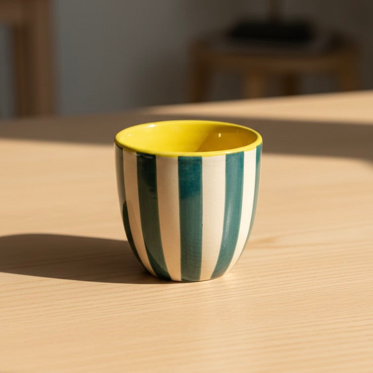 Striped ceramic cup with yellow interior on a wooden surface