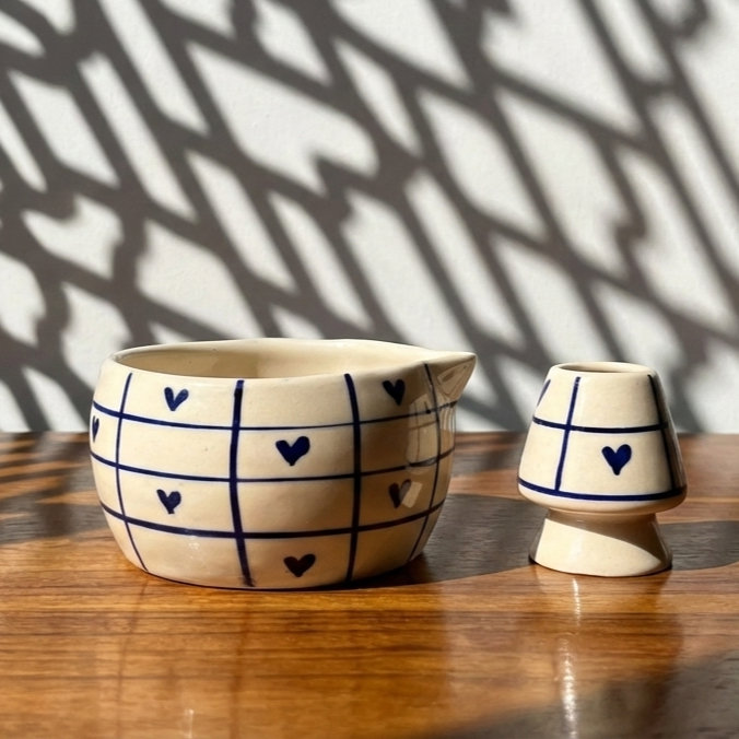 Ceramic matcha bowl and whisk stand with heart and grid pattern on a wooden surface.