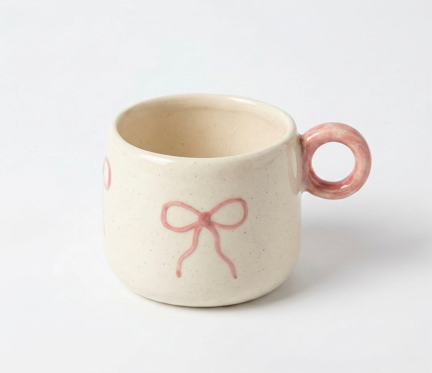 Ceramic mug with pink handle and bow design on a white background