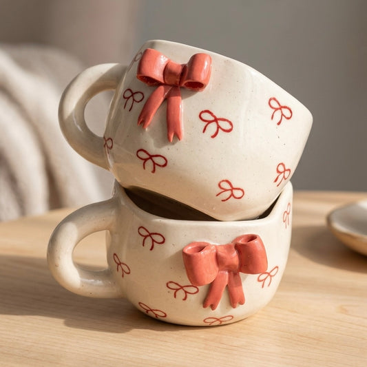 Two ceramic mugs with bow designs stacked on a wooden surface.